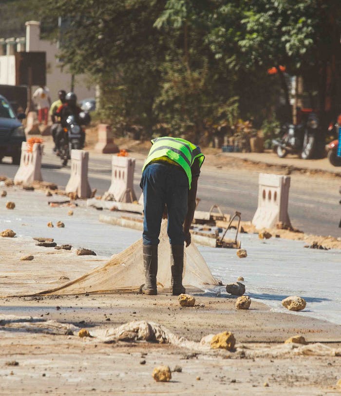 A construction worker in a safety vest working on a road with traffic and barriers.