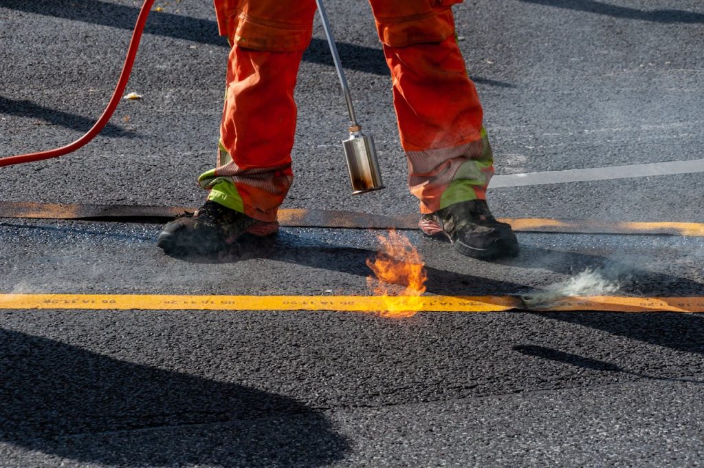 A construction worker using a torch to seal a road's asphalt surface with precision and care.