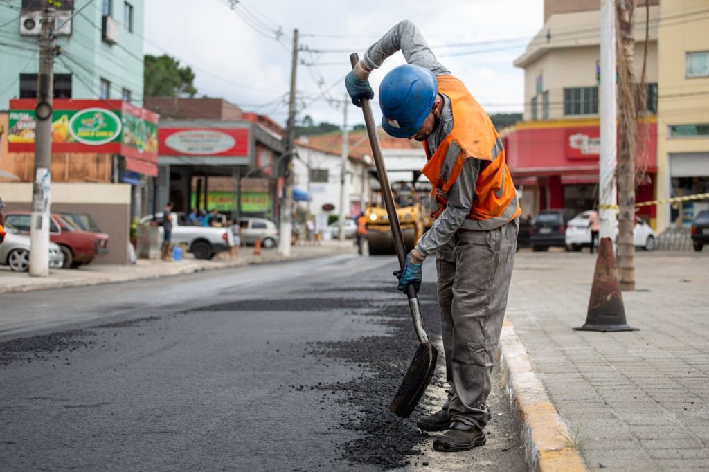 A construction worker paving a street in Cotia, Brazil, using a shovel during the day.